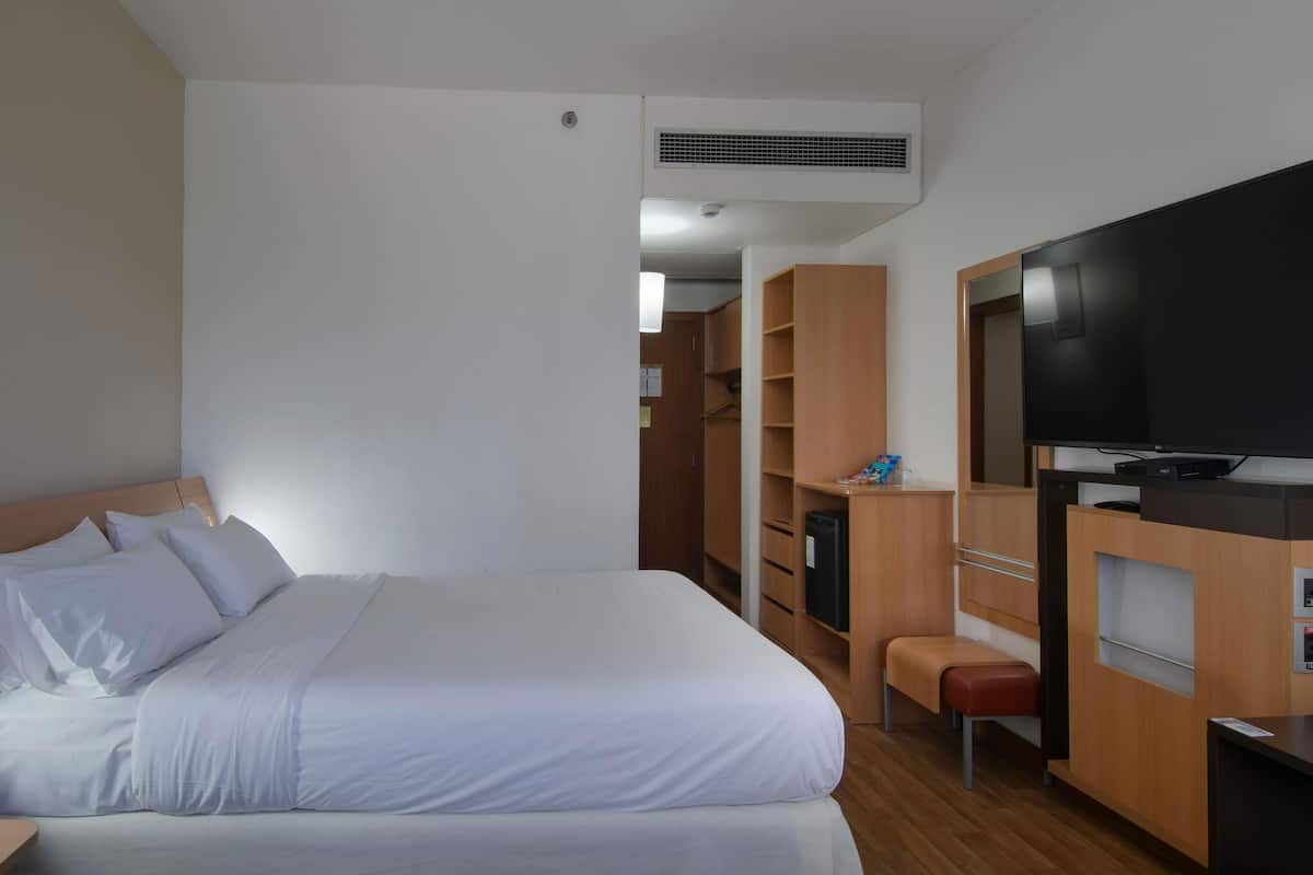A hotel room with a bed, a TV, wooden furniture, and a wardrobe.