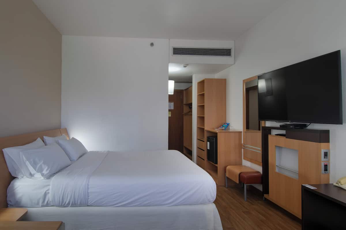 A hotel room with a bed, a TV, a desk, and a wardrobe.