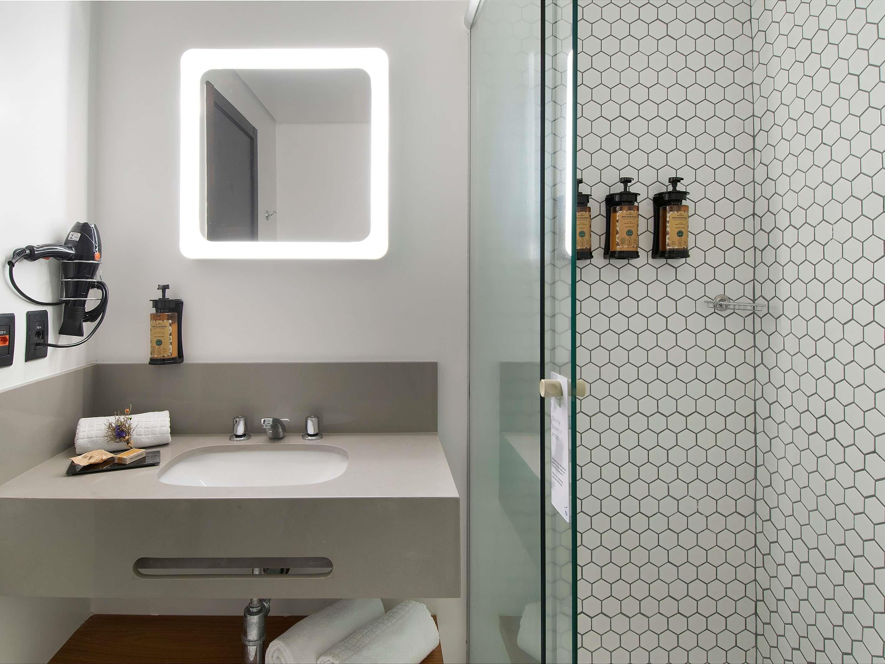A modern bathroom with a large mirror, a hairdryer, and toiletries on the counter.