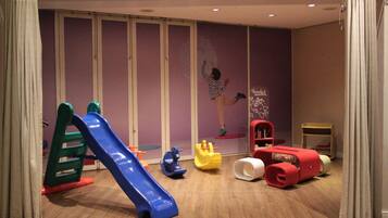 A children's play area with a blue slide, various toys, and a wall with a poster.