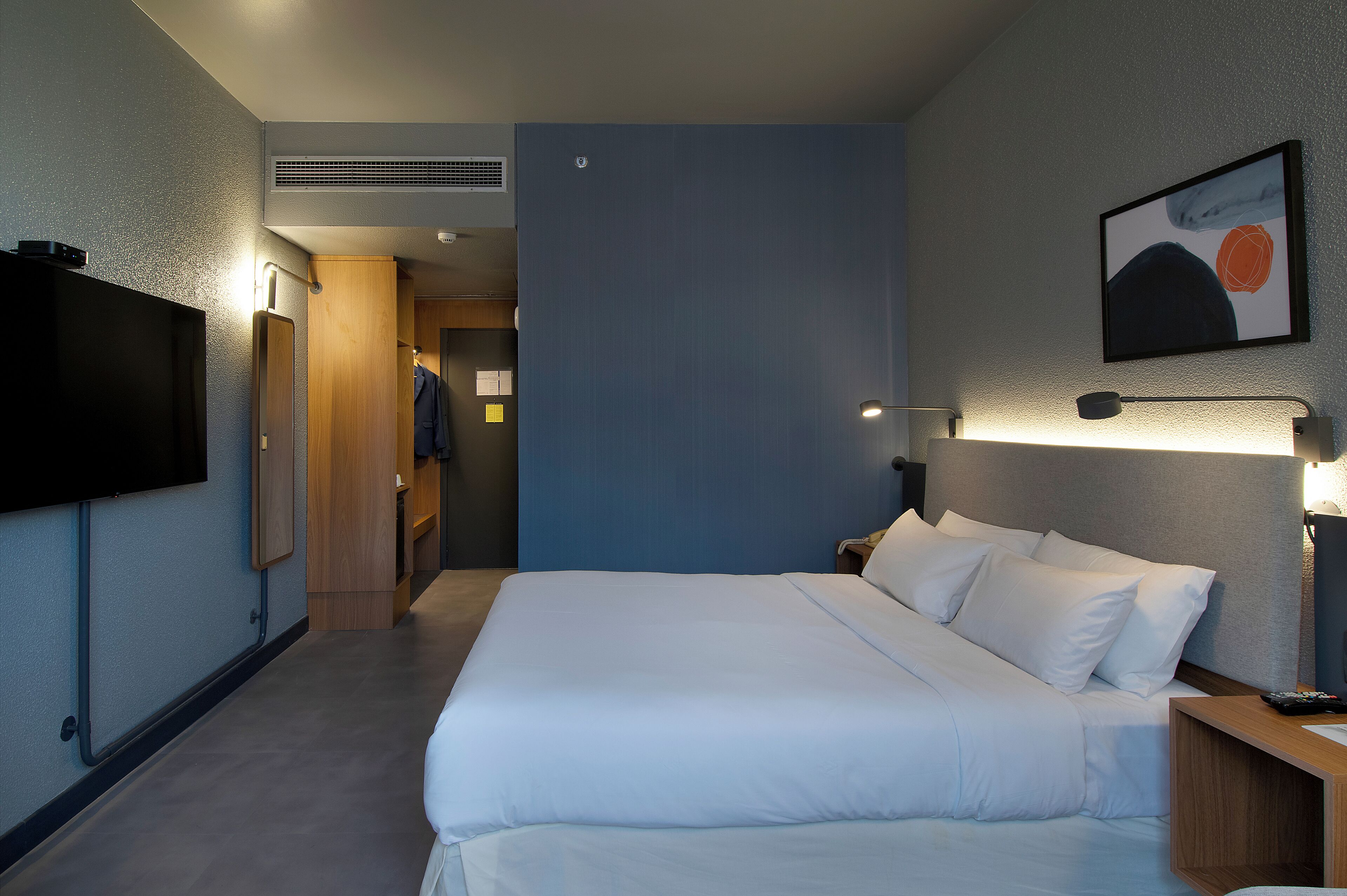 Ein Hotelzimmer mit einem großen Bett, einem flachbildfernseher an der Wand und einem Gemälde über dem Bett.