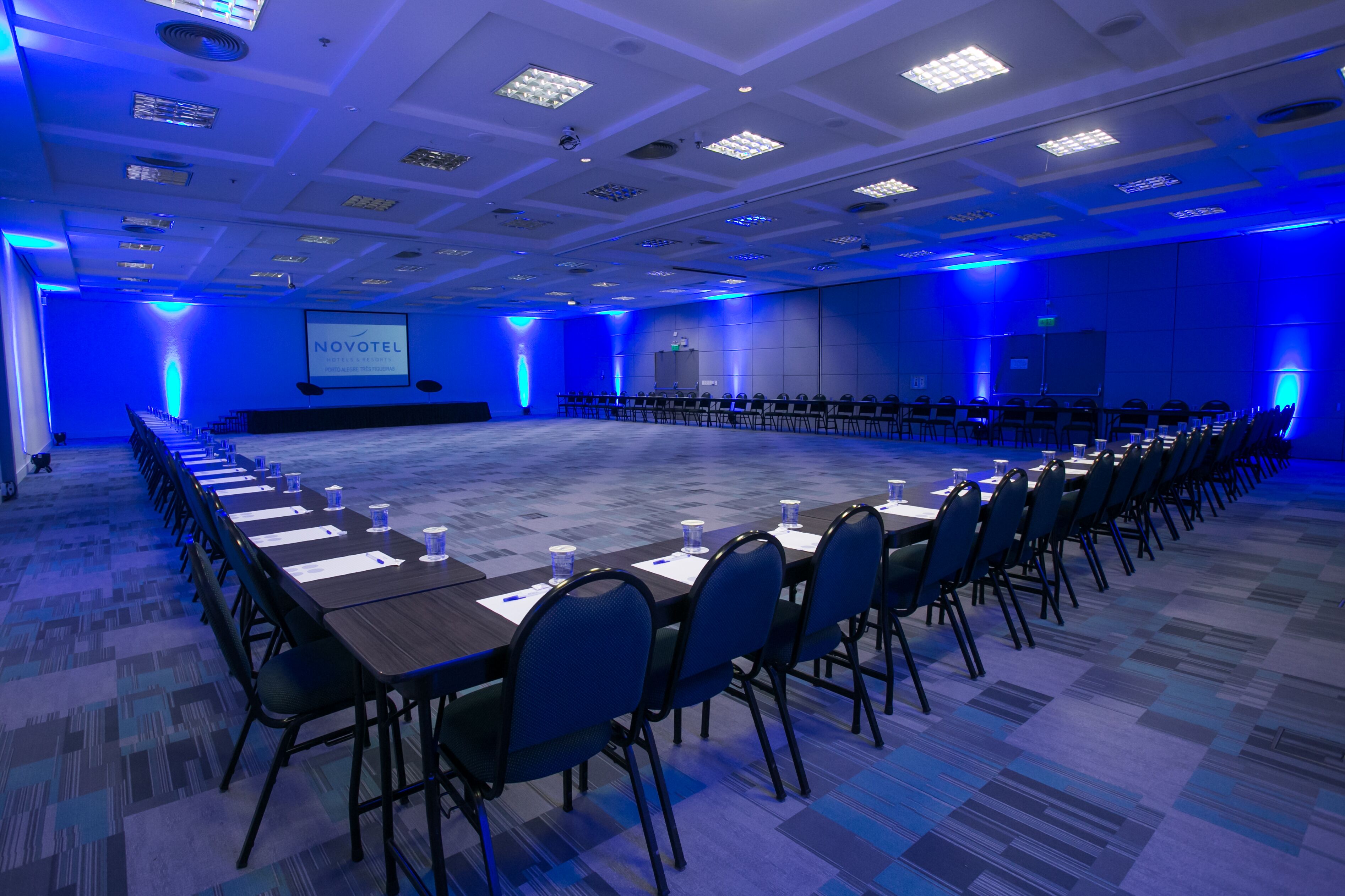 A conference room with a long table, chairs, and a screen displaying "NOVOTEL".