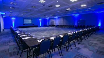 A conference room with a long table, chairs, and a screen displaying "NOVOTEL".