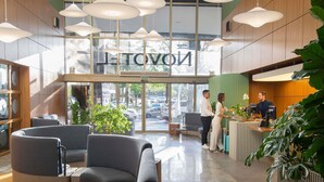 A hotel lobby with seating, a reception desk, and a large window with the hotel's name. - Novotel Porto Alegre Tres Figueiras Hotel (Porto Alegre)