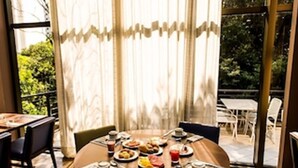 A dining area with a round table, chairs, and a view of greenery through large windows. - Novotel Porto Alegre Tres Figueiras Hotel (Porto Alegre)