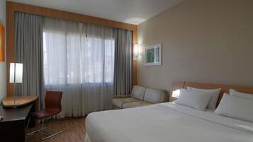 Et hotelværelse med seng, skrivebord, stol og sofa.