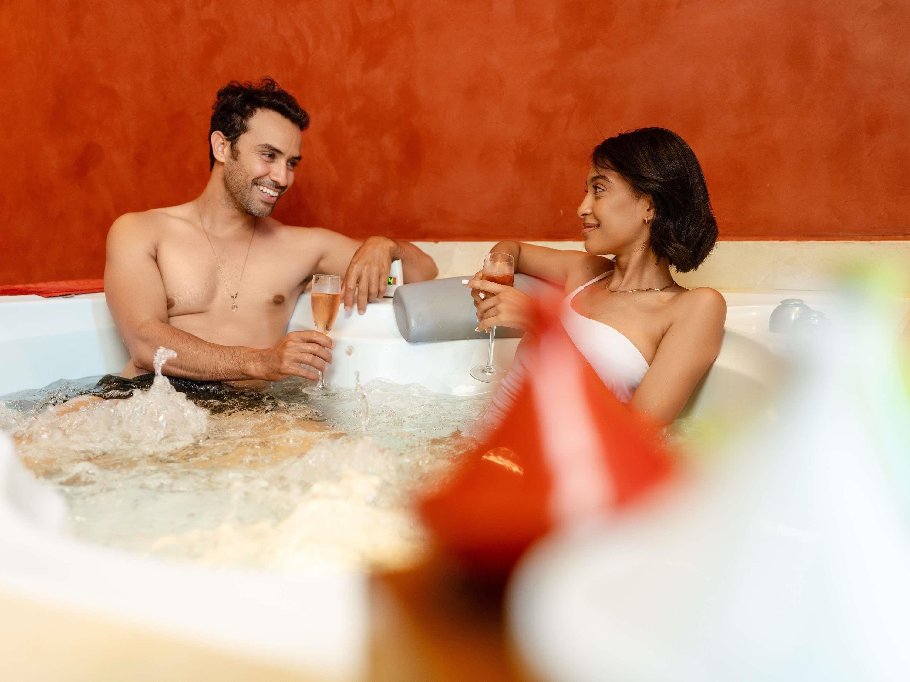 A couple in a hot tub with bubbles, a glass of drink, and a red object in the foreground.