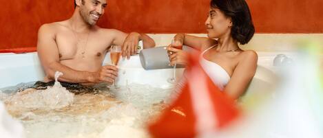 A couple in a hot tub with bubbles, a glass of drink, and a red object in the foreground.