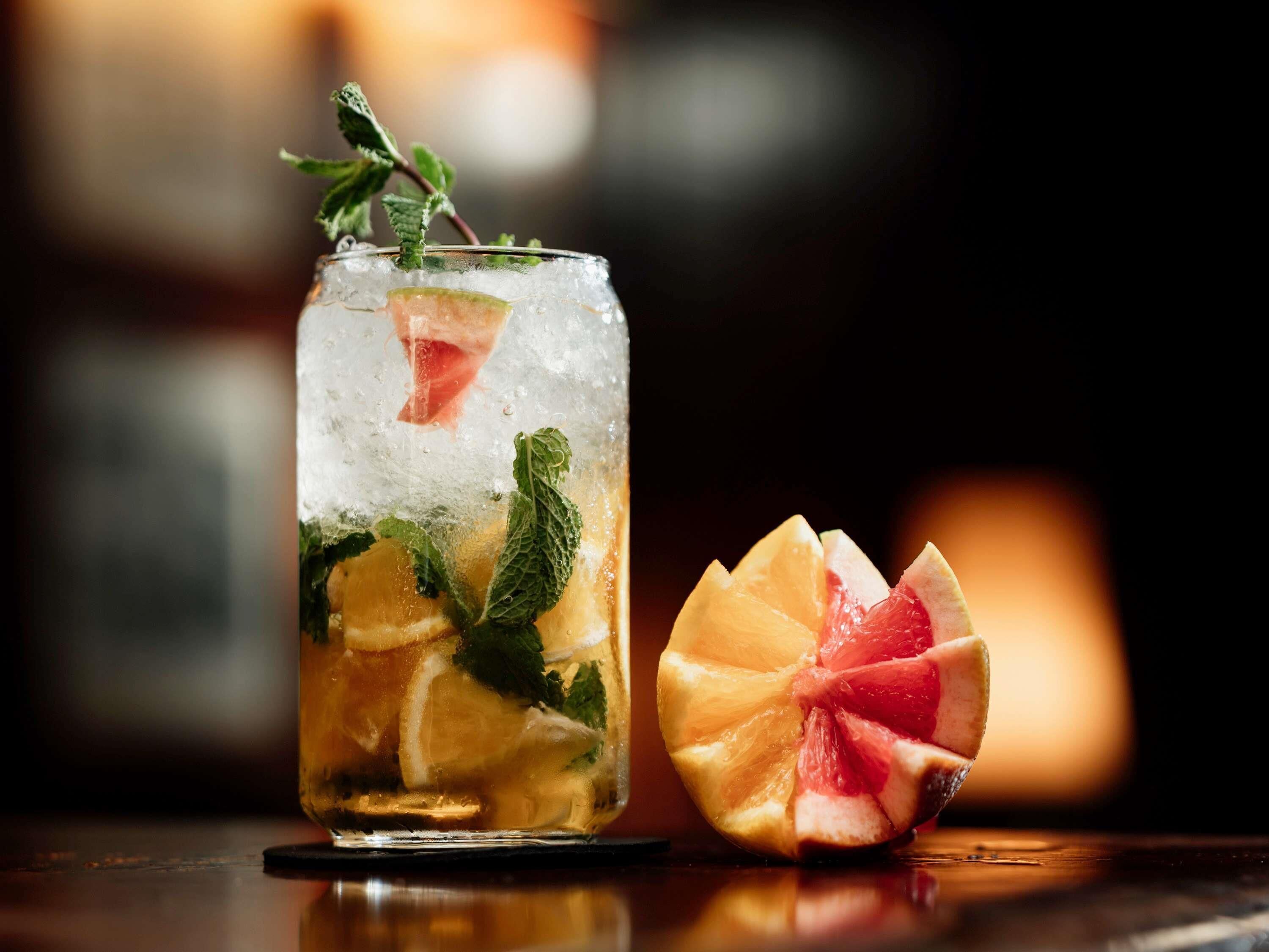 A glass of cocktail with ice, mint leaves, and citrus slices.