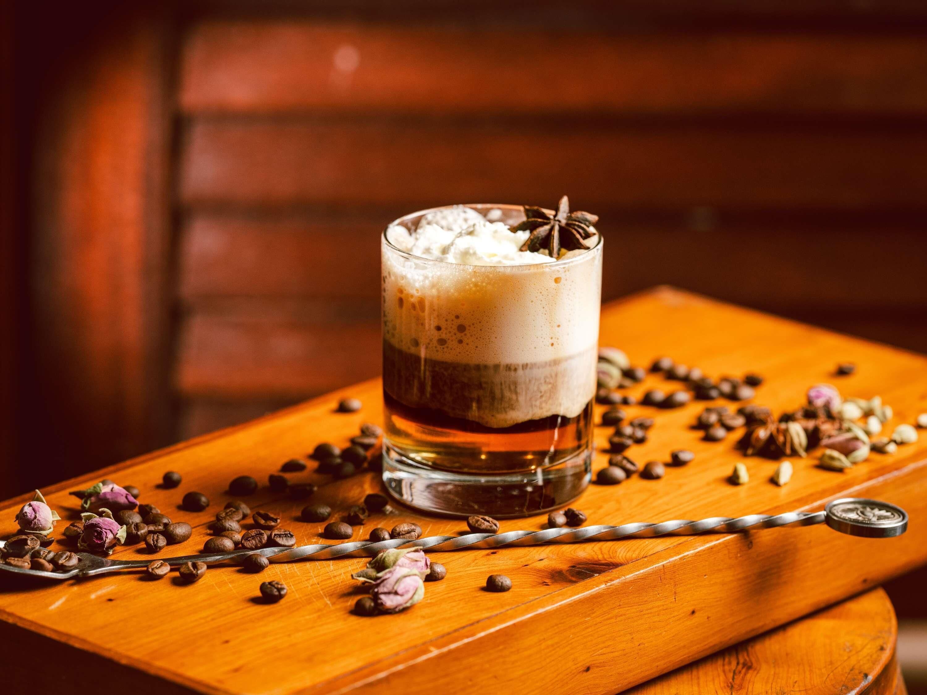Un vaso de bebida en capas con granos de café y una estrella de anís sobre una superficie de madera.
