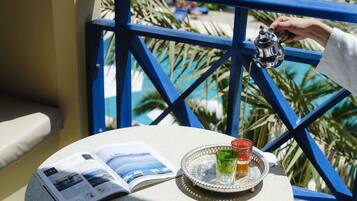 A table with a magazine, a tray with glasses, and a teapot on a balcony with blue railings.