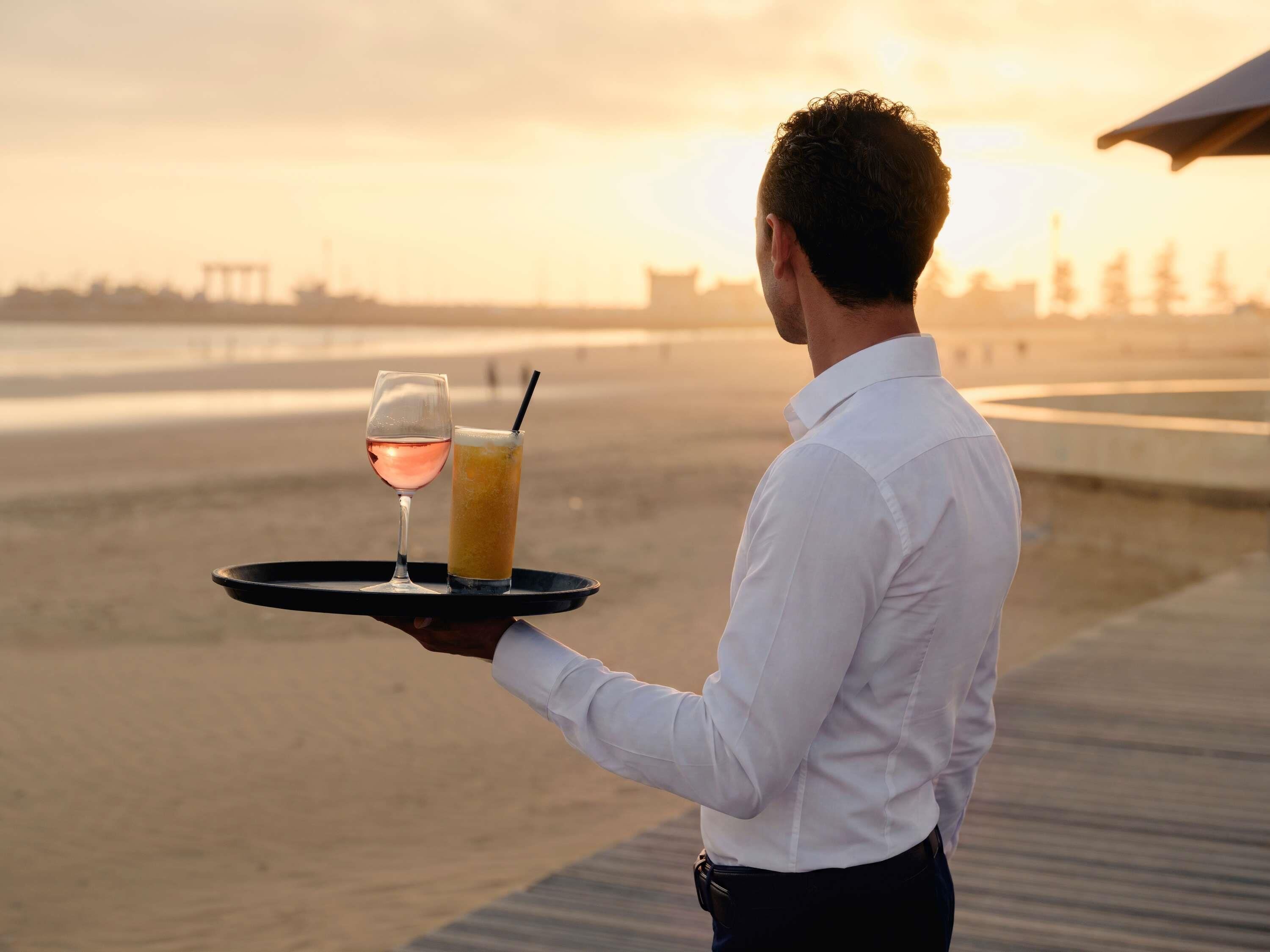 A person holding a tray with a glass of wine and a cocktail.