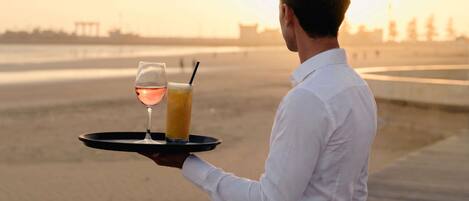 A person holding a tray with a glass of wine and a cocktail.