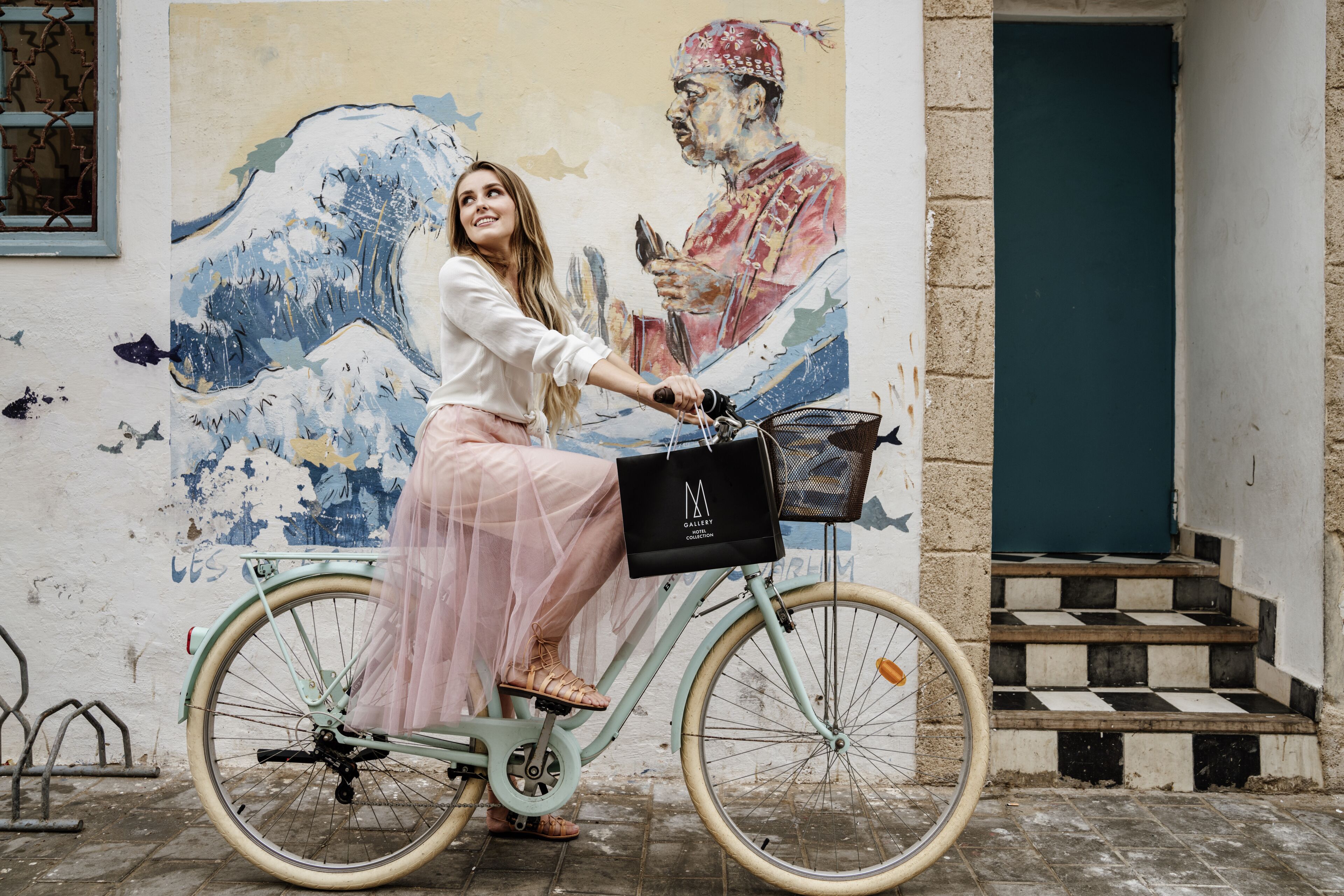 Una bicicleta antigua con cesta y alforja, estacionada frente a un mural.