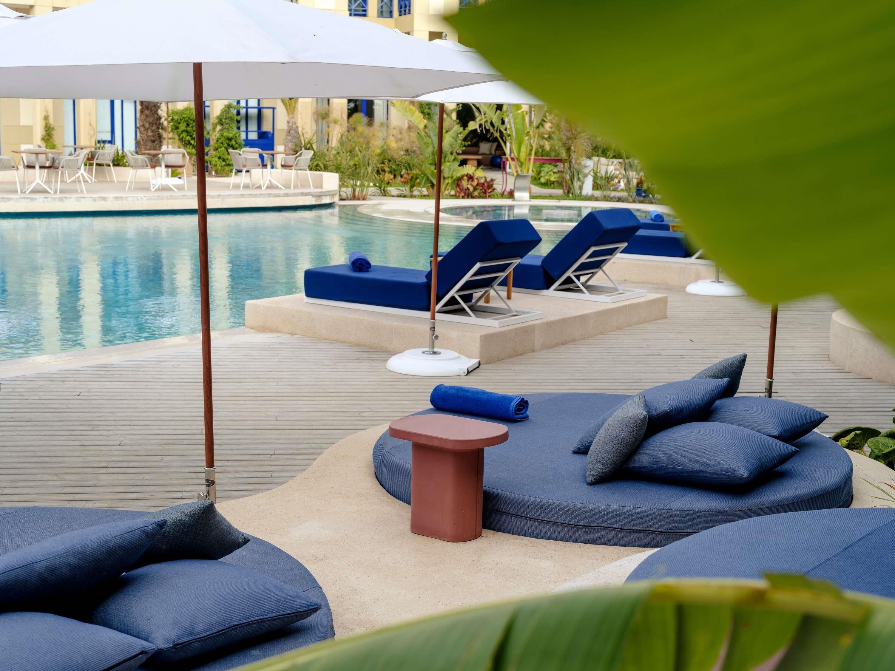 A poolside area with lounge chairs and umbrellas, a small table, and a pool.