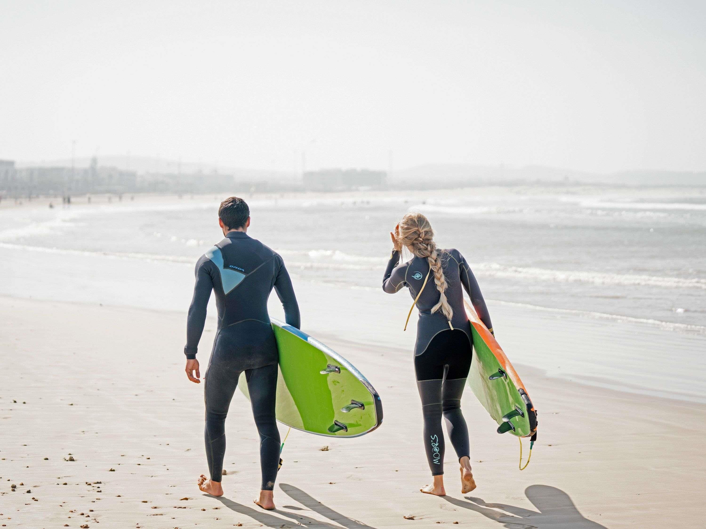Two individuals walking on a beach with surfboards, wearing wetsuits.