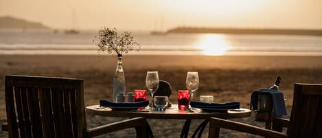 A table set for two with a view of the beach and sunset.