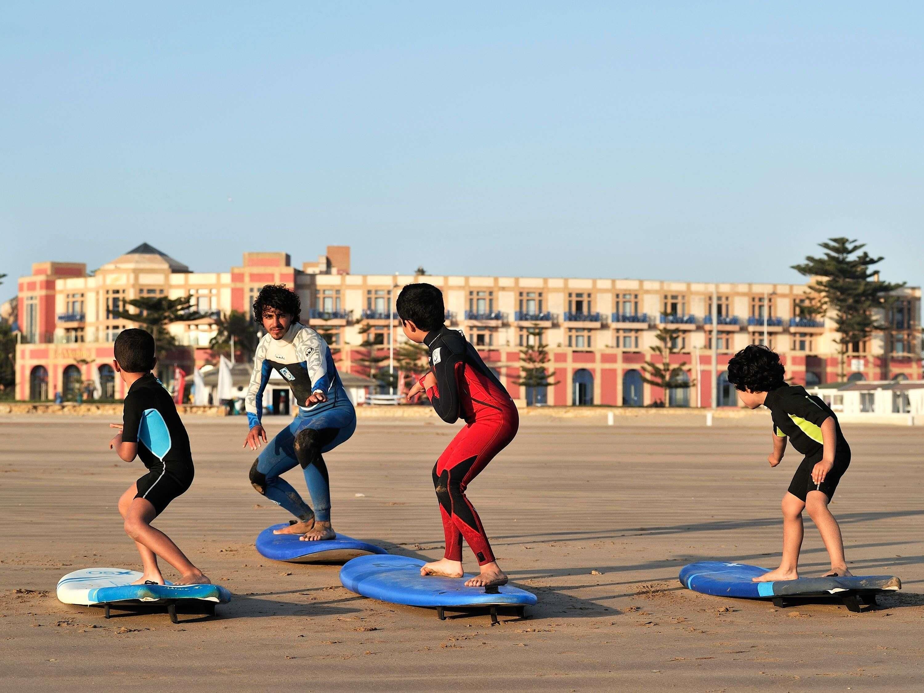 Four individuals practicing on balance boards on a sandy surface with a building in the background.