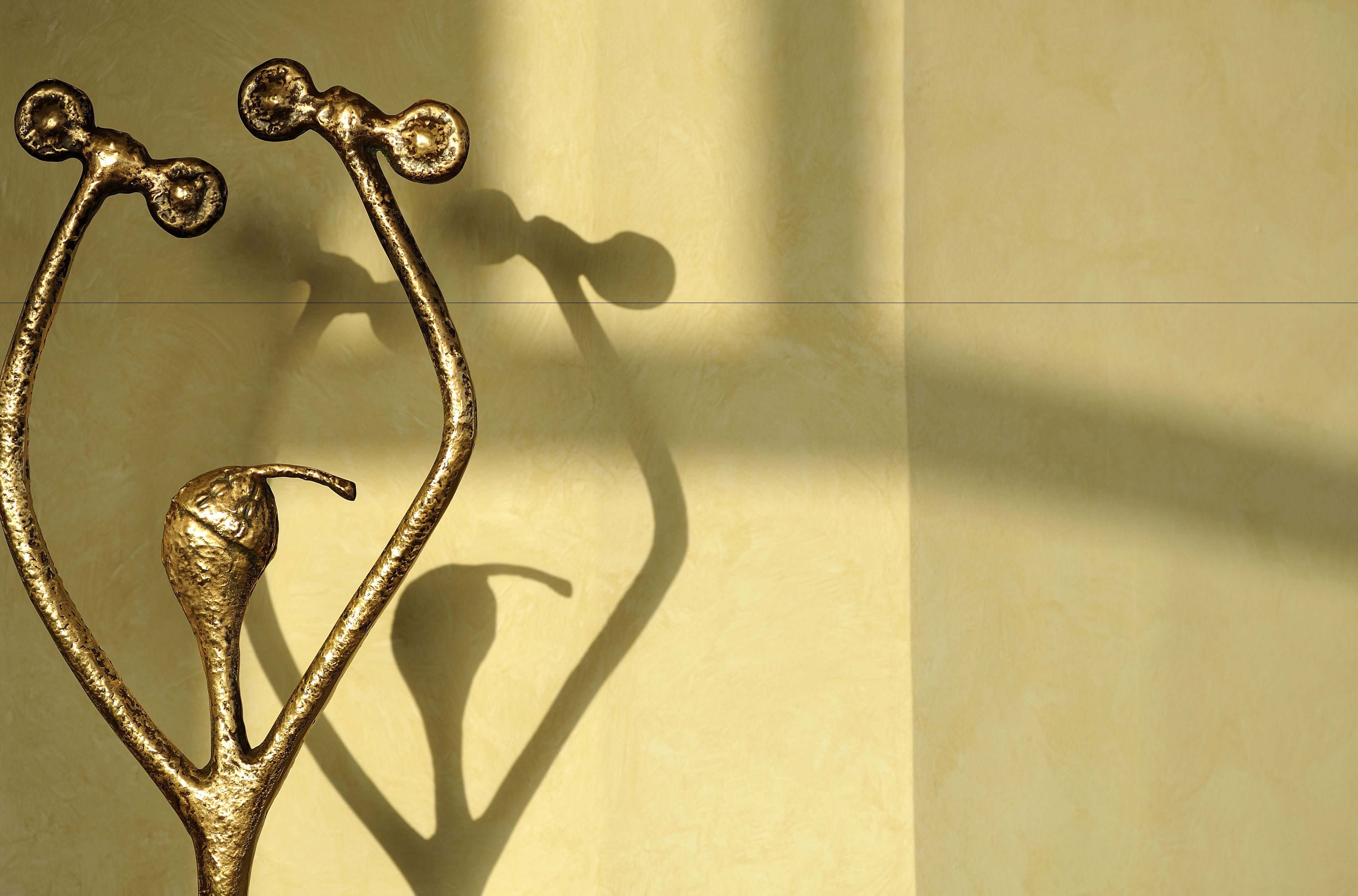 Een metalen sculptuur met een vogel en twee gebogen elementen voor een effen muur.