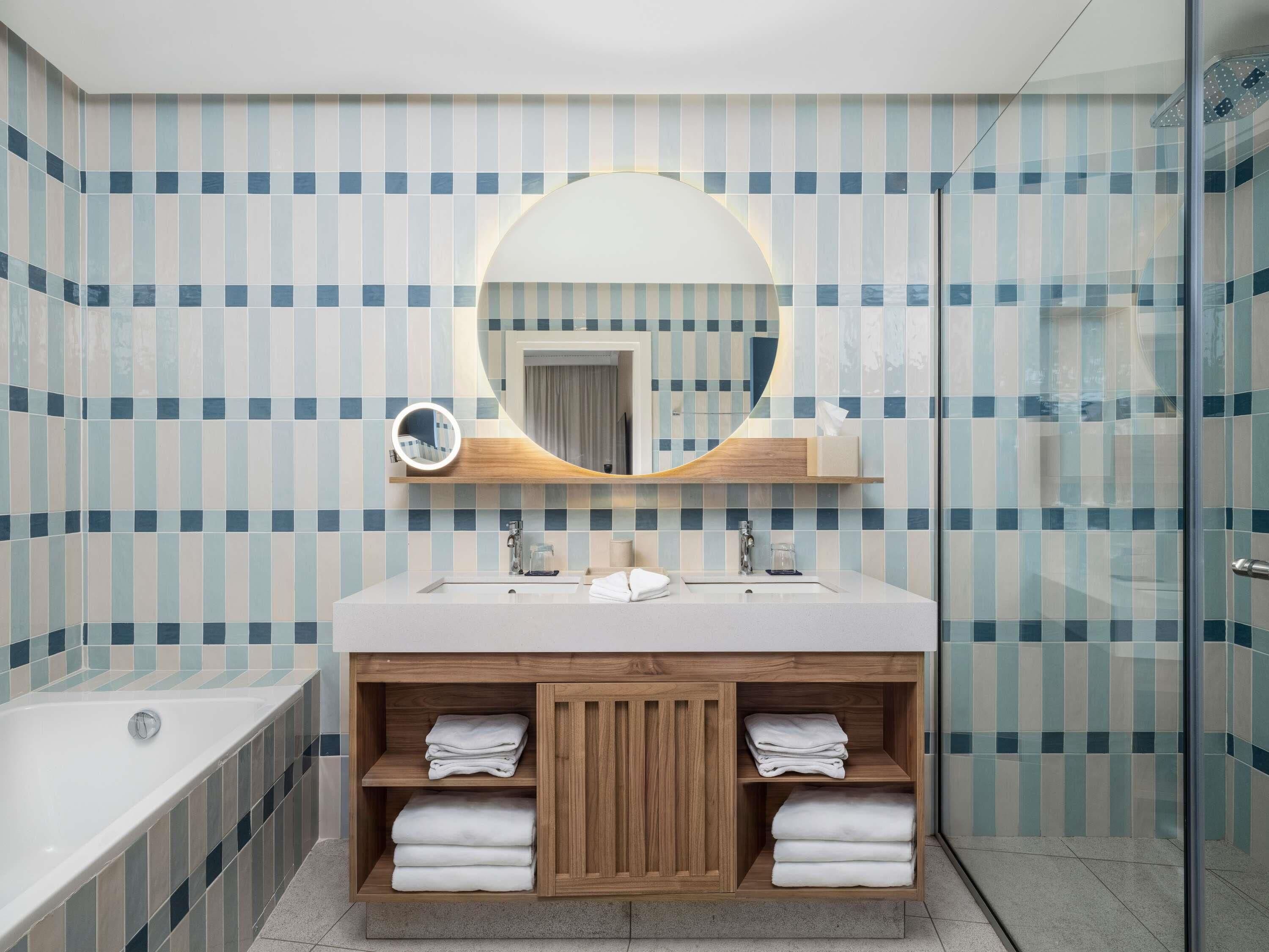 Un baño moderno con un espejo grande, una bañera y un tocador con estantes.