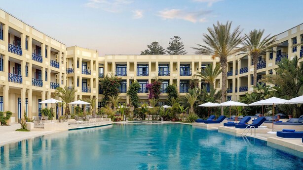 A hotel with a swimming pool, lounge chairs, and a multi-story building with balconies. - Le Médina Essaouira Thalassa Sea  & Spa - MGallery Collection (Essaouira)