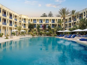 Un hotel con piscina, sillones de descanso y un edificio de varios pisos con balcones.