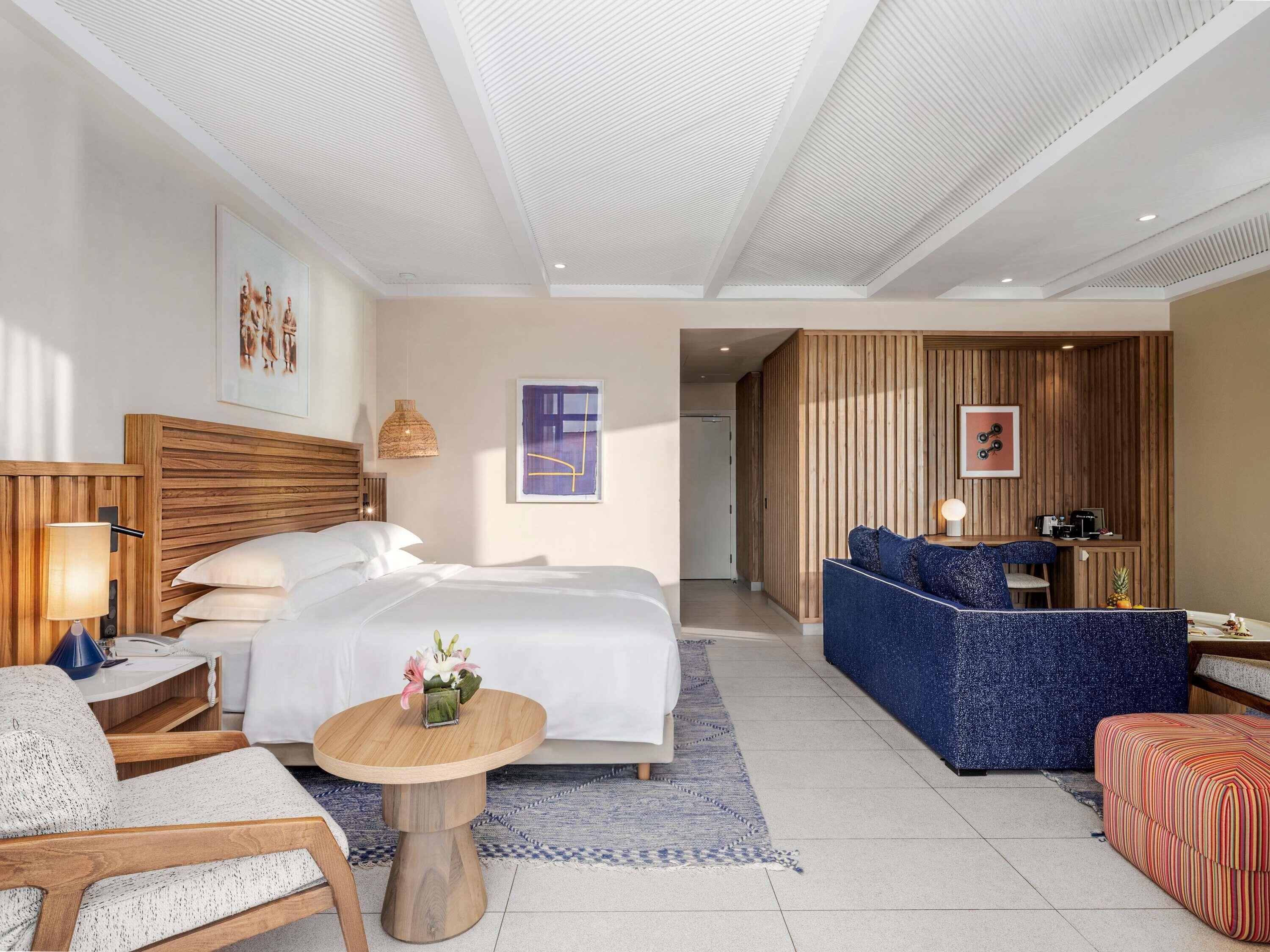 Une chambre d’hôtel comprenant un lit, un canapé, une chaise, une petite table et un bureau avec une lampe.