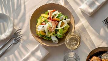 Une table avec une assiette de salade, un verre de vin blanc et un panier de pain.