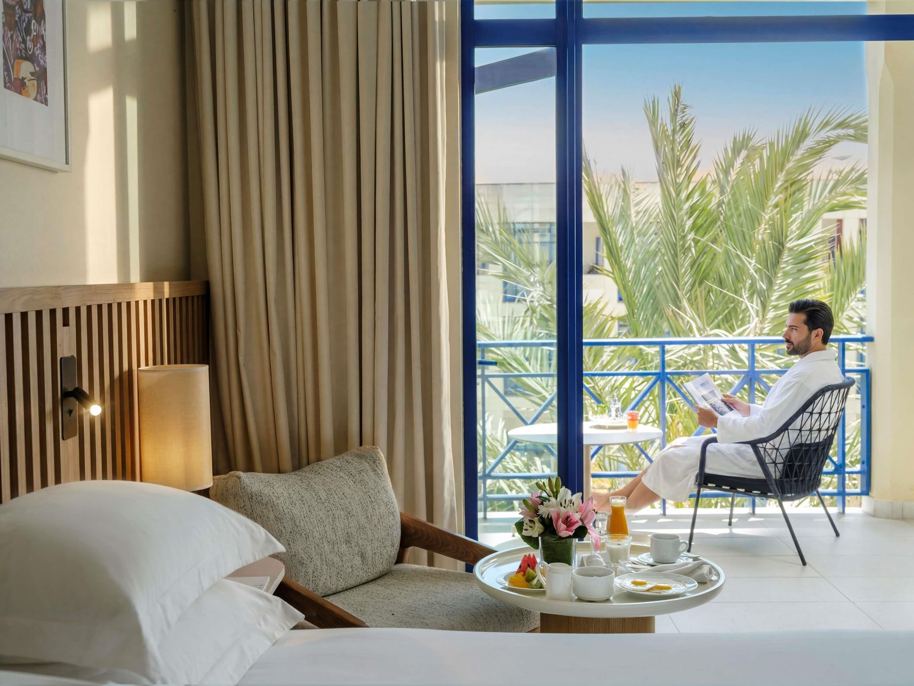 Une chambre d’hôtel avec un balcon, un lit, une chaise et un plateau de petit-déjeuner.