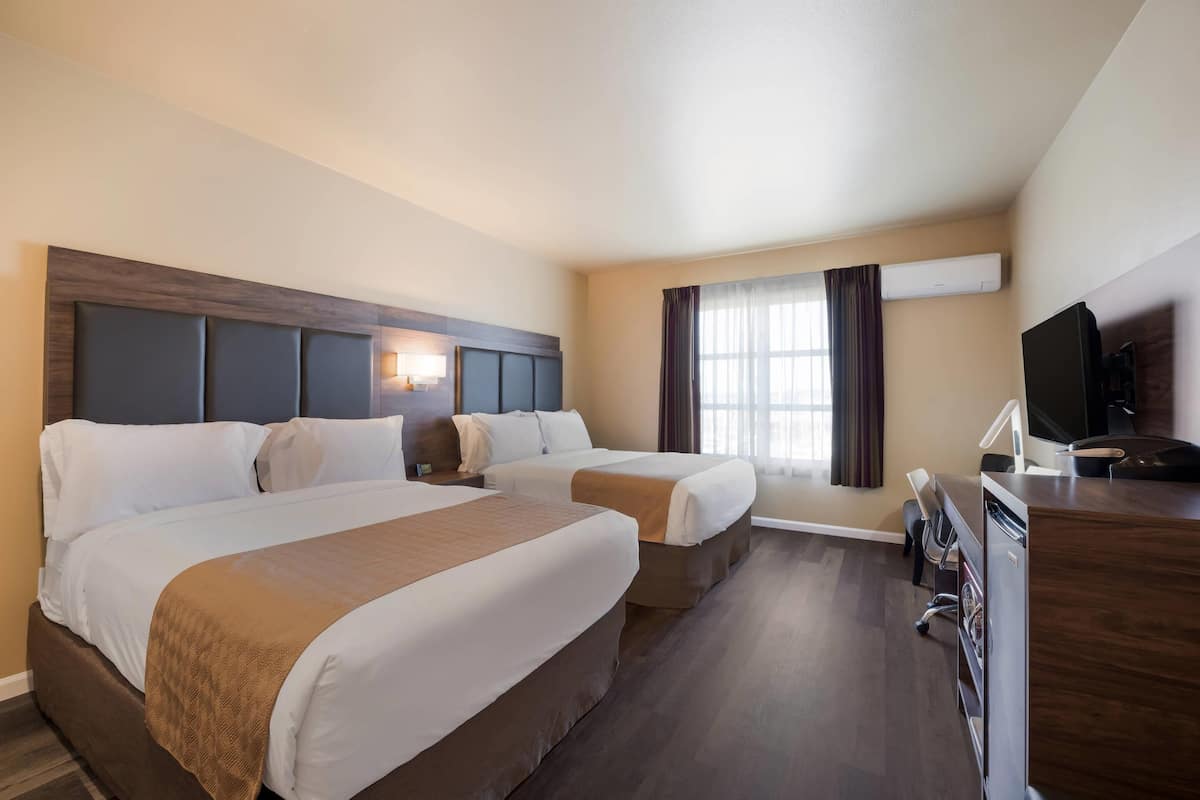 A hotel room with two beds, a desk, a TV, and an air conditioning unit.
