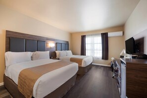 A hotel room with two beds, a desk, a TV, and an air conditioning unit.