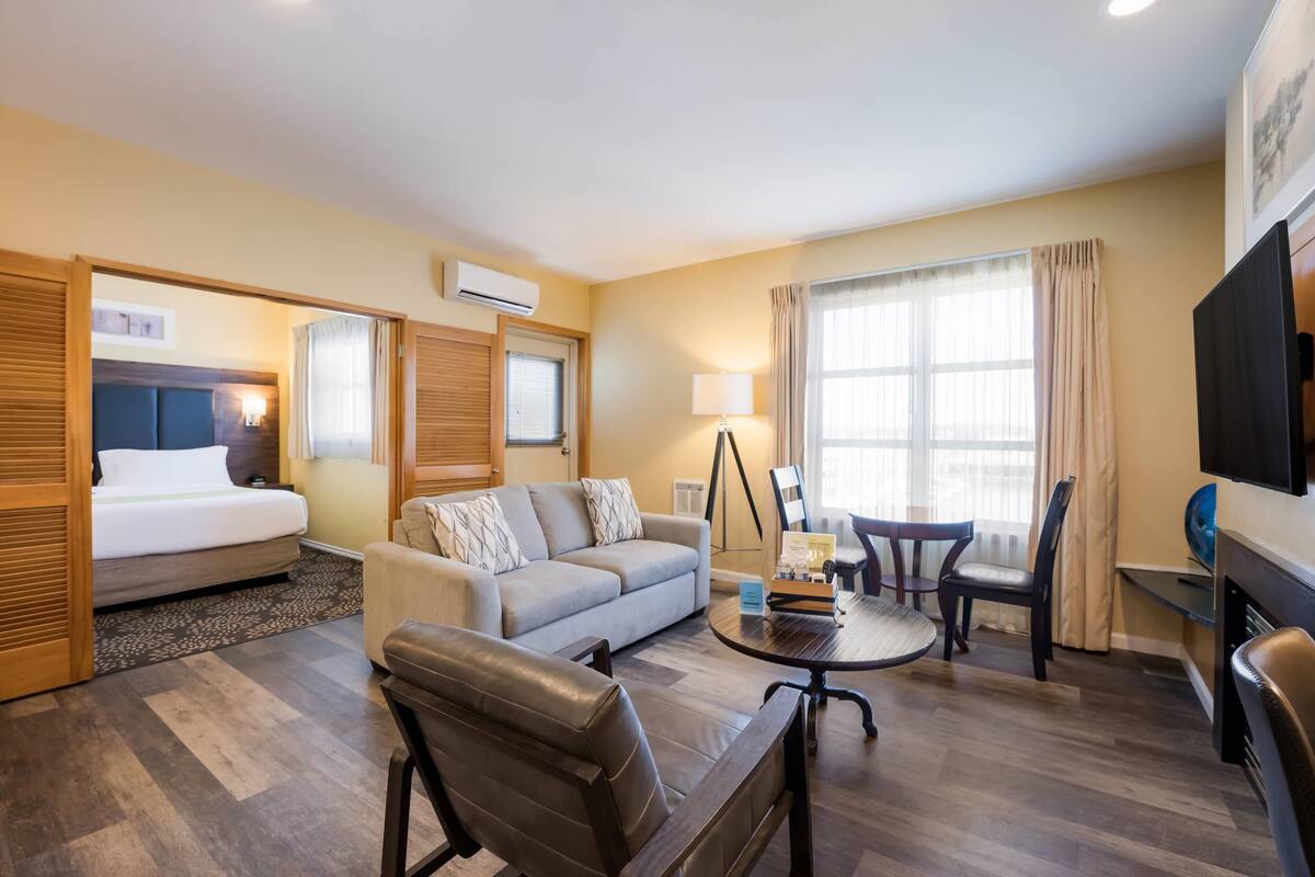 A hotel room with a bed, sofa, coffee table, chairs, and a TV.