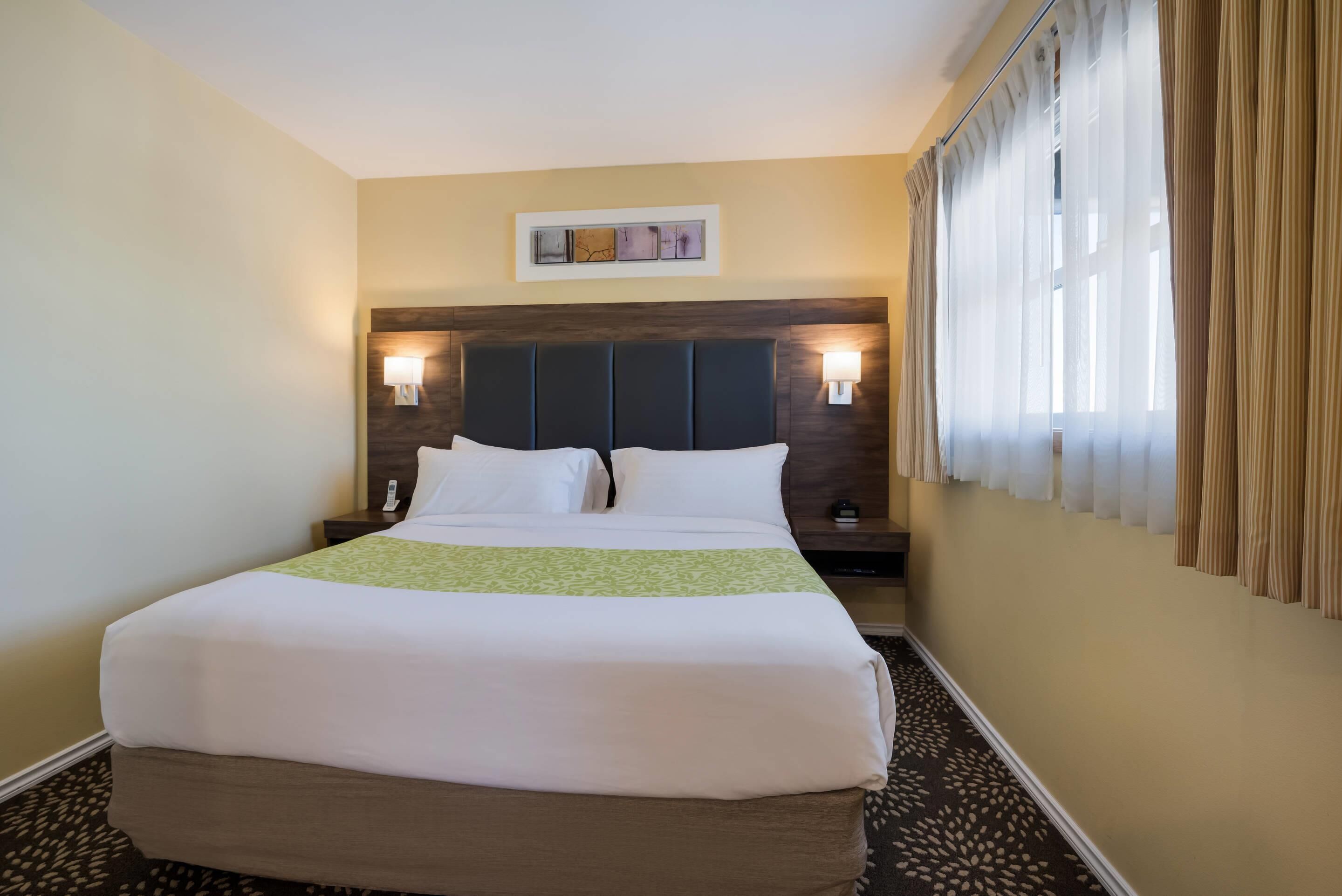 Une chambre d’hôtel avec un grand lit, deux tables de chevet, une tête de lit et une fenêtre avec des rideaux.