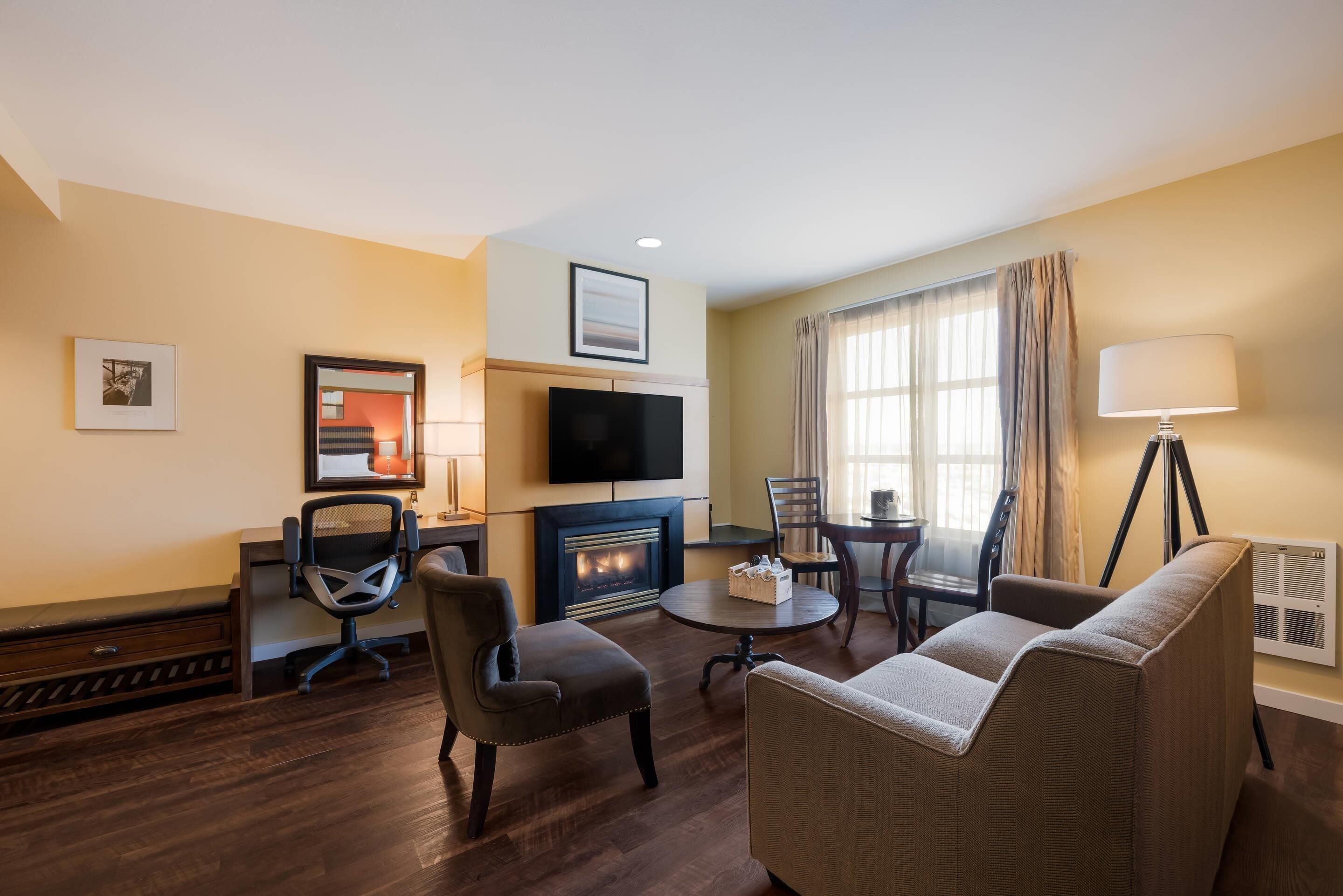 A hotel room with a fireplace, a television, a dining table with chairs, a sofa, and a lamp.