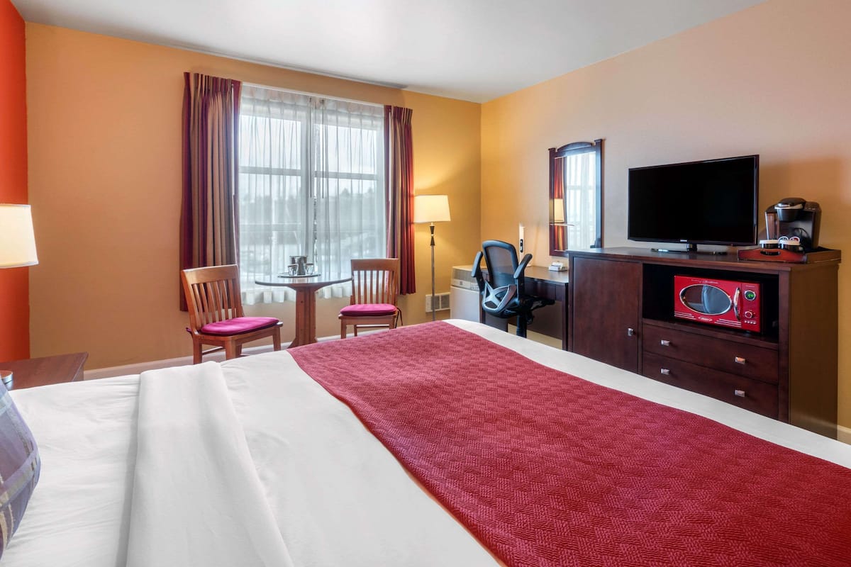 A hotel room with a large bed, a desk with a chair, a television, and a microwave.