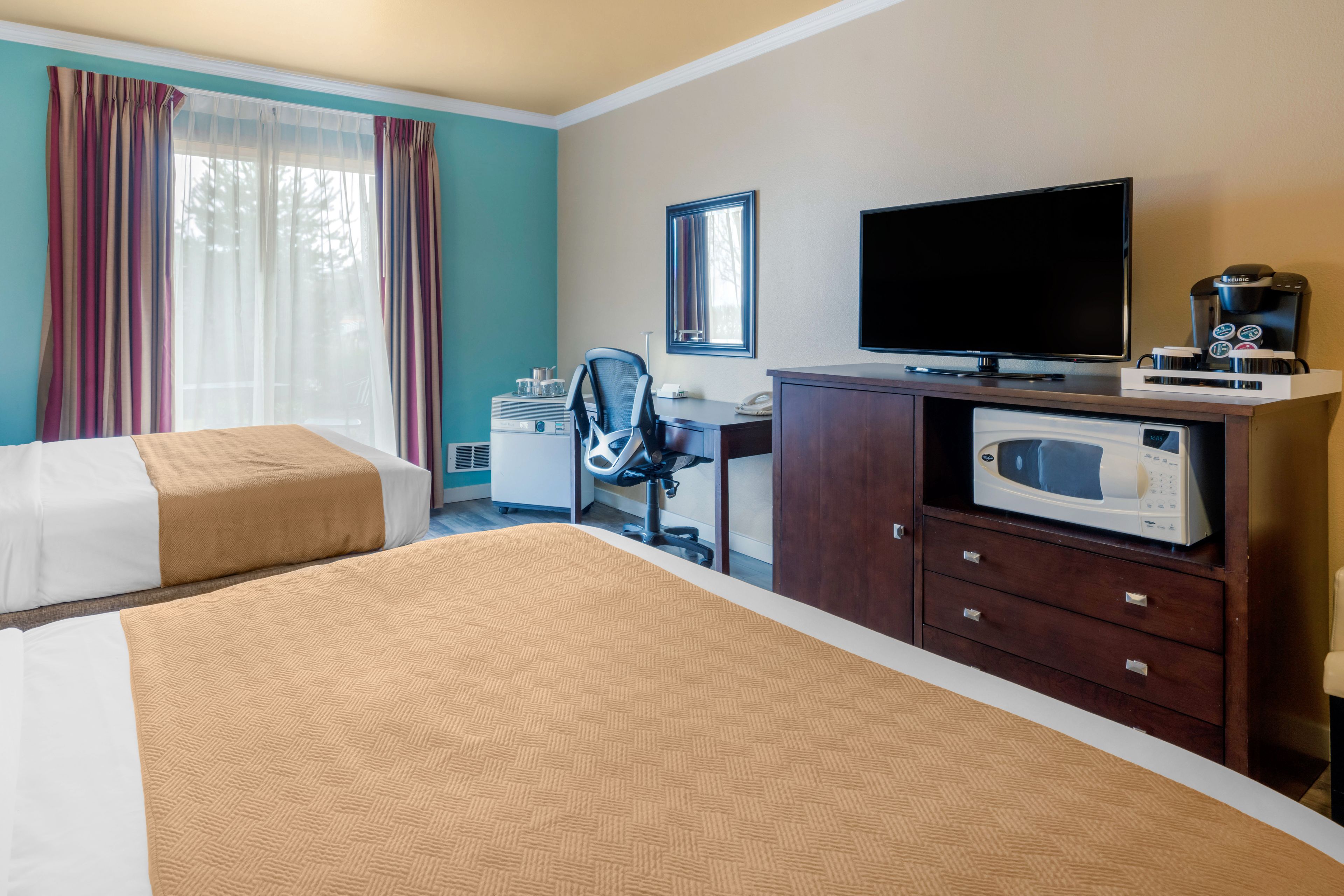 A hotel room with two beds, a desk with a computer, a television, a microwave, and a coffee maker.