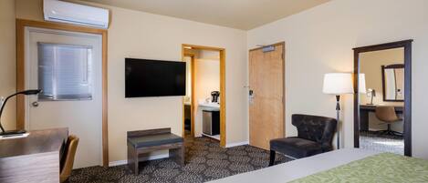 Une chambre d’hôtel avec un lit, un bureau, une chaise, une télévision et une salle de bain visible à travers une porte ouverte.