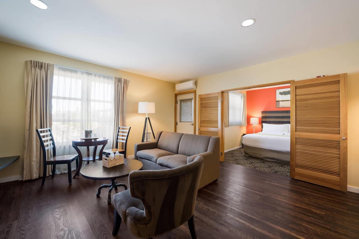 A hotel room with a sofa, two armchairs, a small table, a lamp, a bed, and a wooden wardrobe.