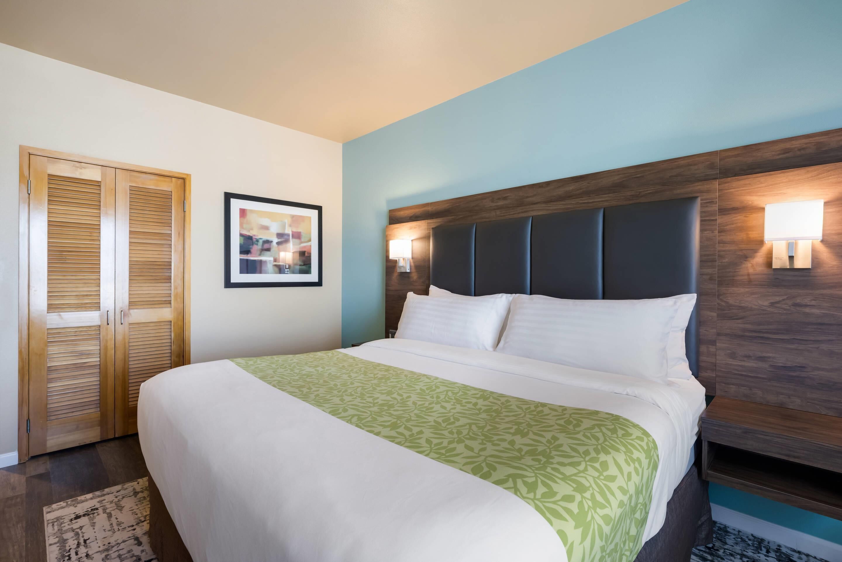 A hotel room with a bed, wooden wardrobe, and a framed picture on the wall.
