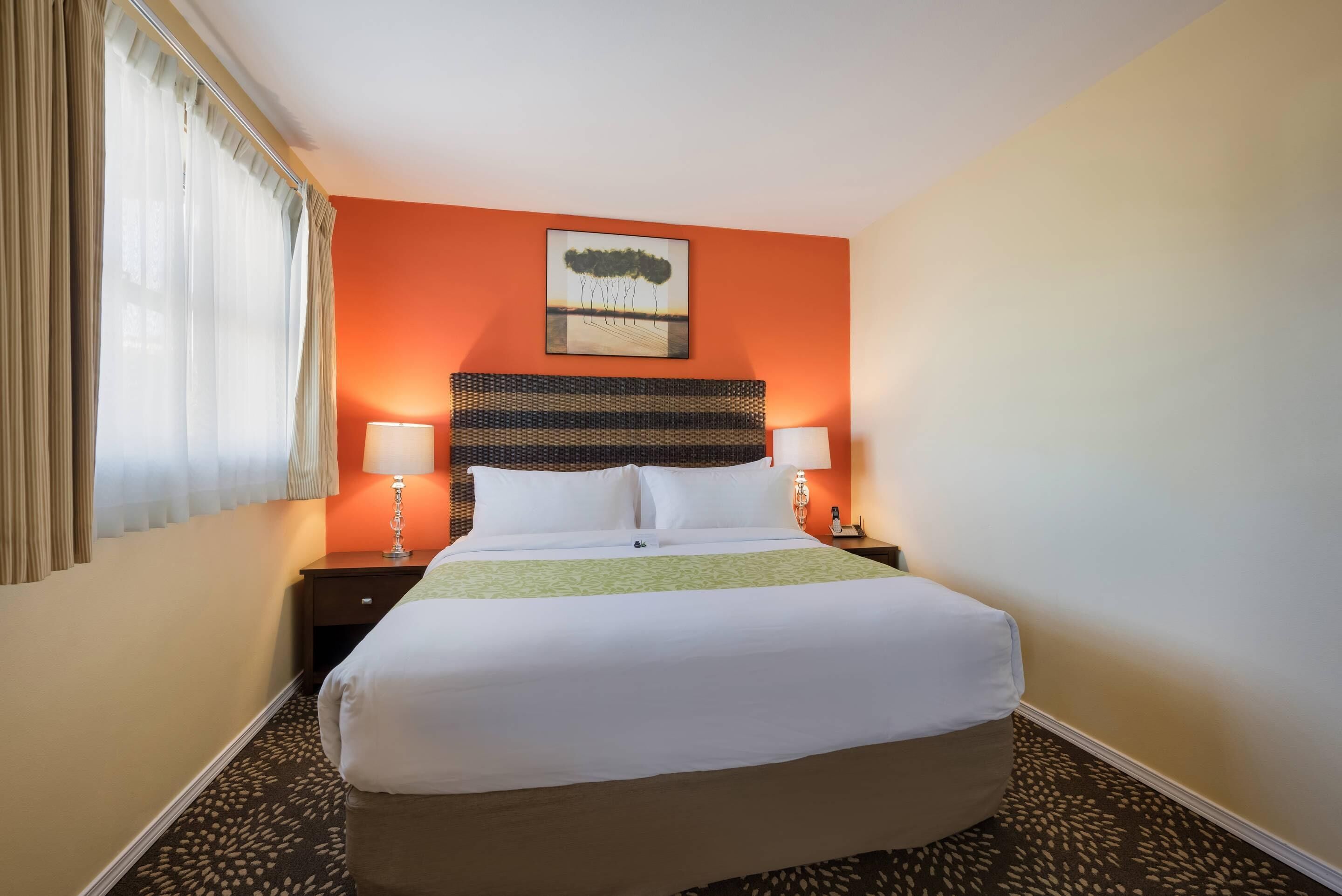 A hotel room with a large bed, two bedside tables, a lamp on each table, and a painting on the wall.