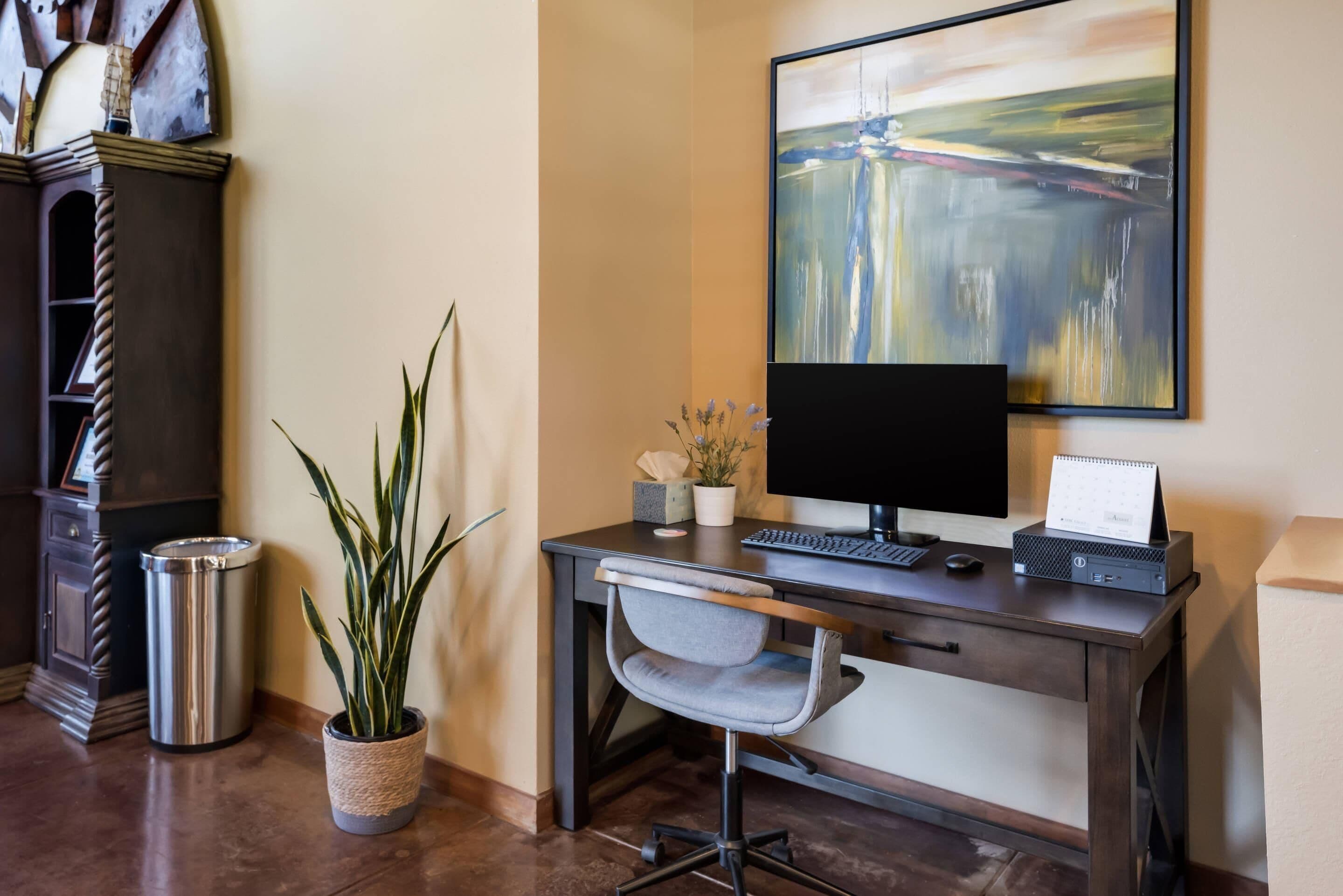 A home office setup with a desk, chair, computer, and a painting on the wall.
