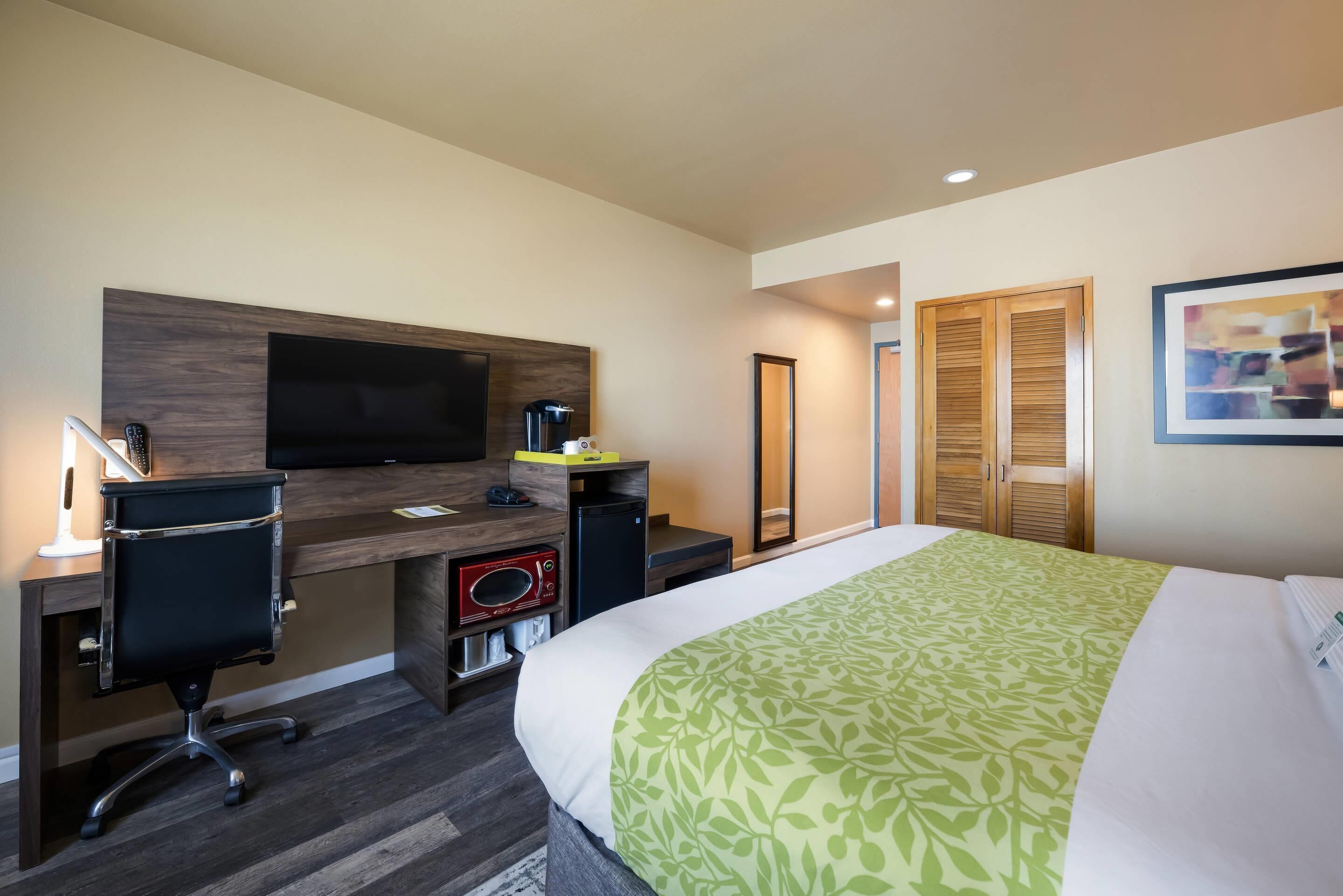 A hotel room with a bed, desk, chair, television, and wardrobe.