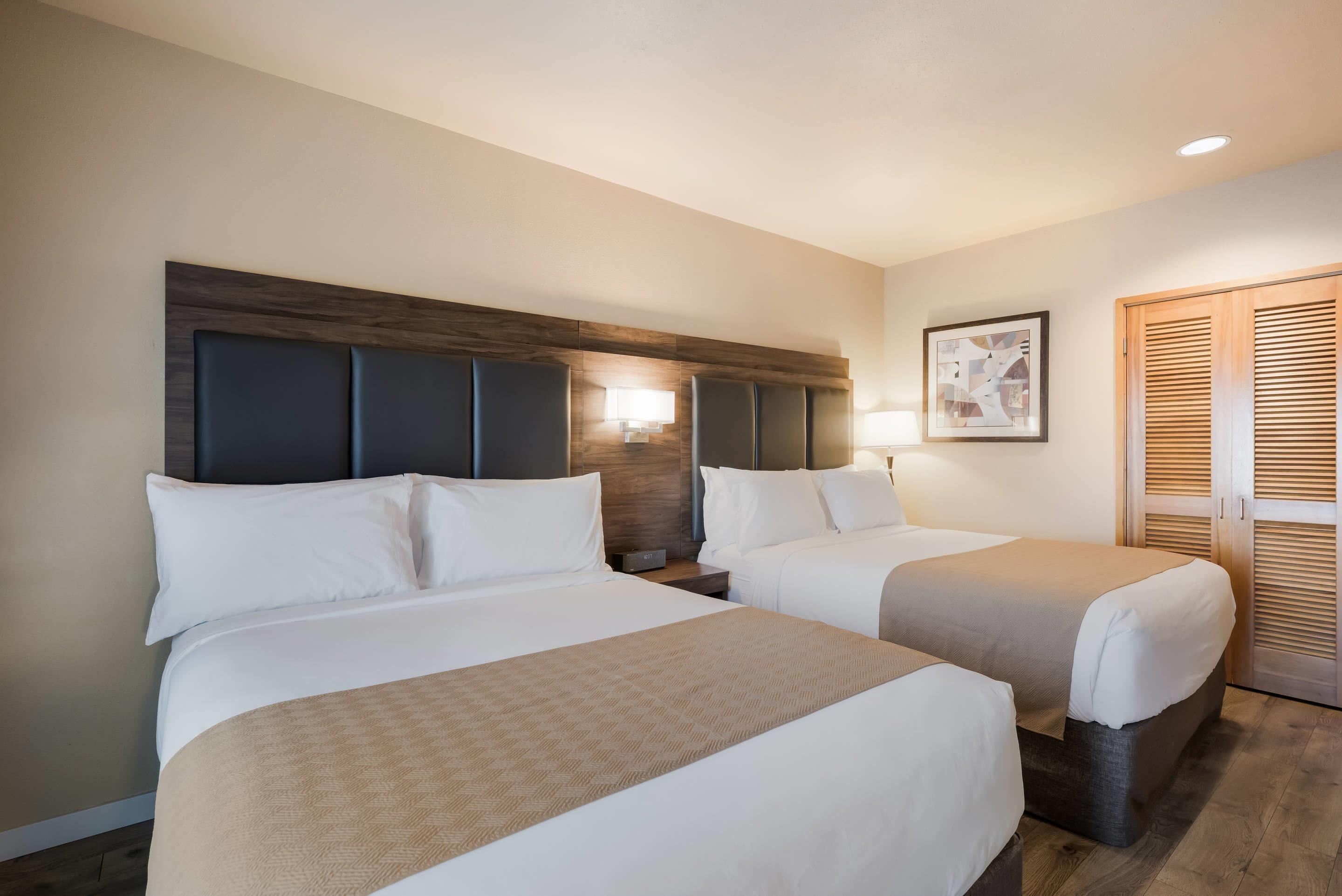 Une chambre d’hôtel avec deux lits, une tête de lit en bois, une table de chevet avec une lampe et une armoire en bois.