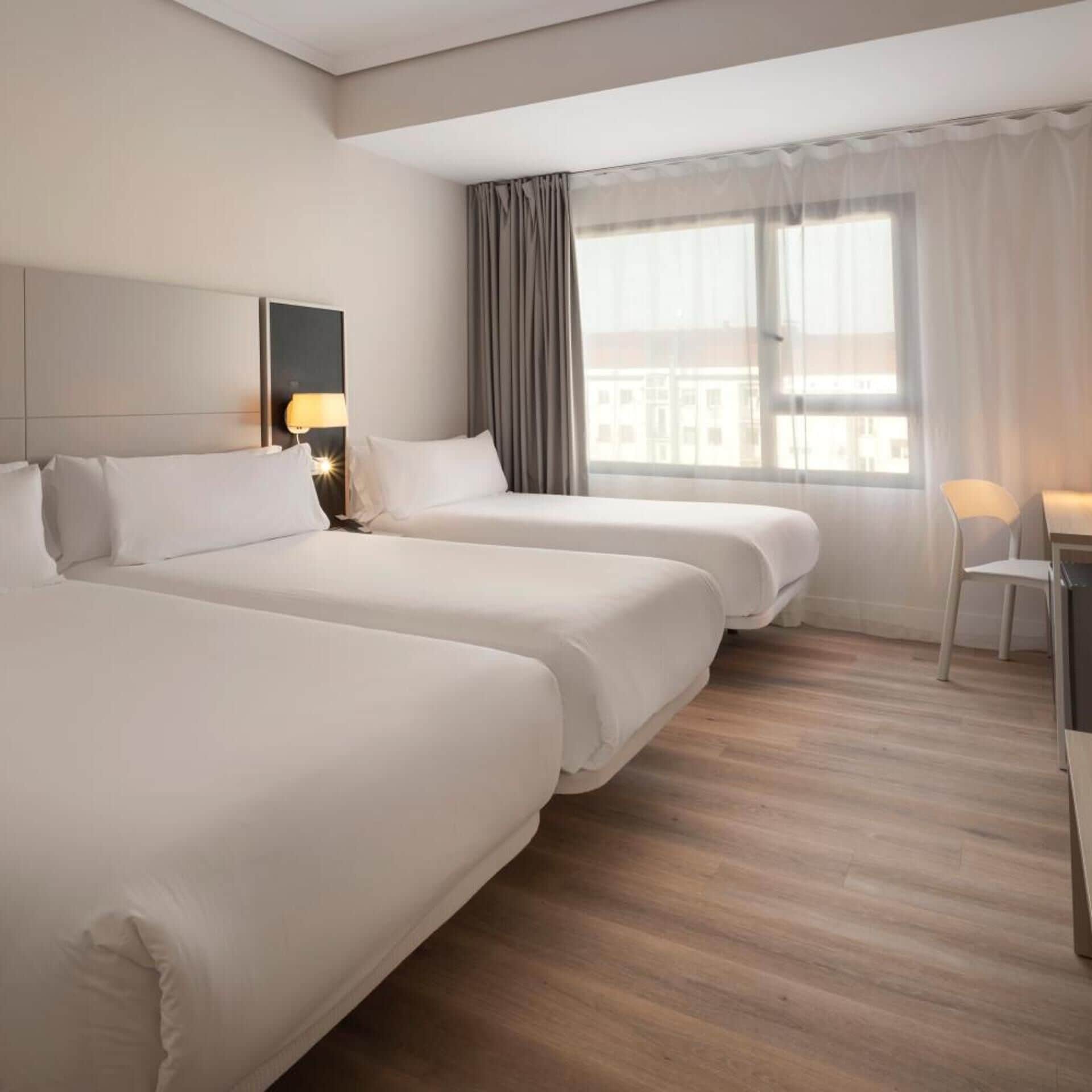 A hotel room with two beds, a desk, and a chair.