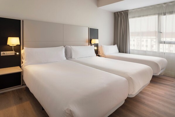 Habitación de hotel con dos camas, una mesita de noche, una lámpara y una ventana con cortinas.