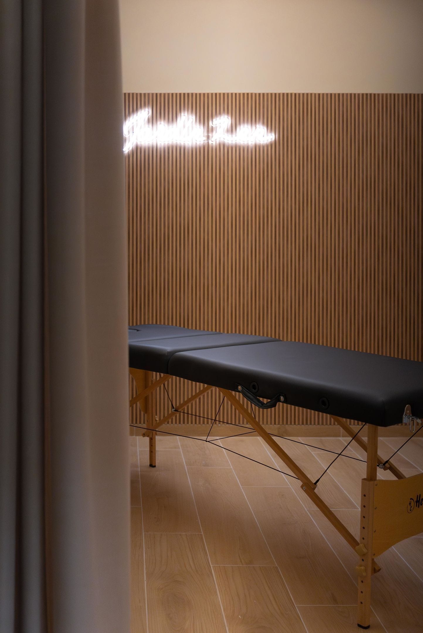 Un mur en bois avec des lattes verticales et une table d’examen noire dans une pièce dont le sol est recouvert de planches de bois.