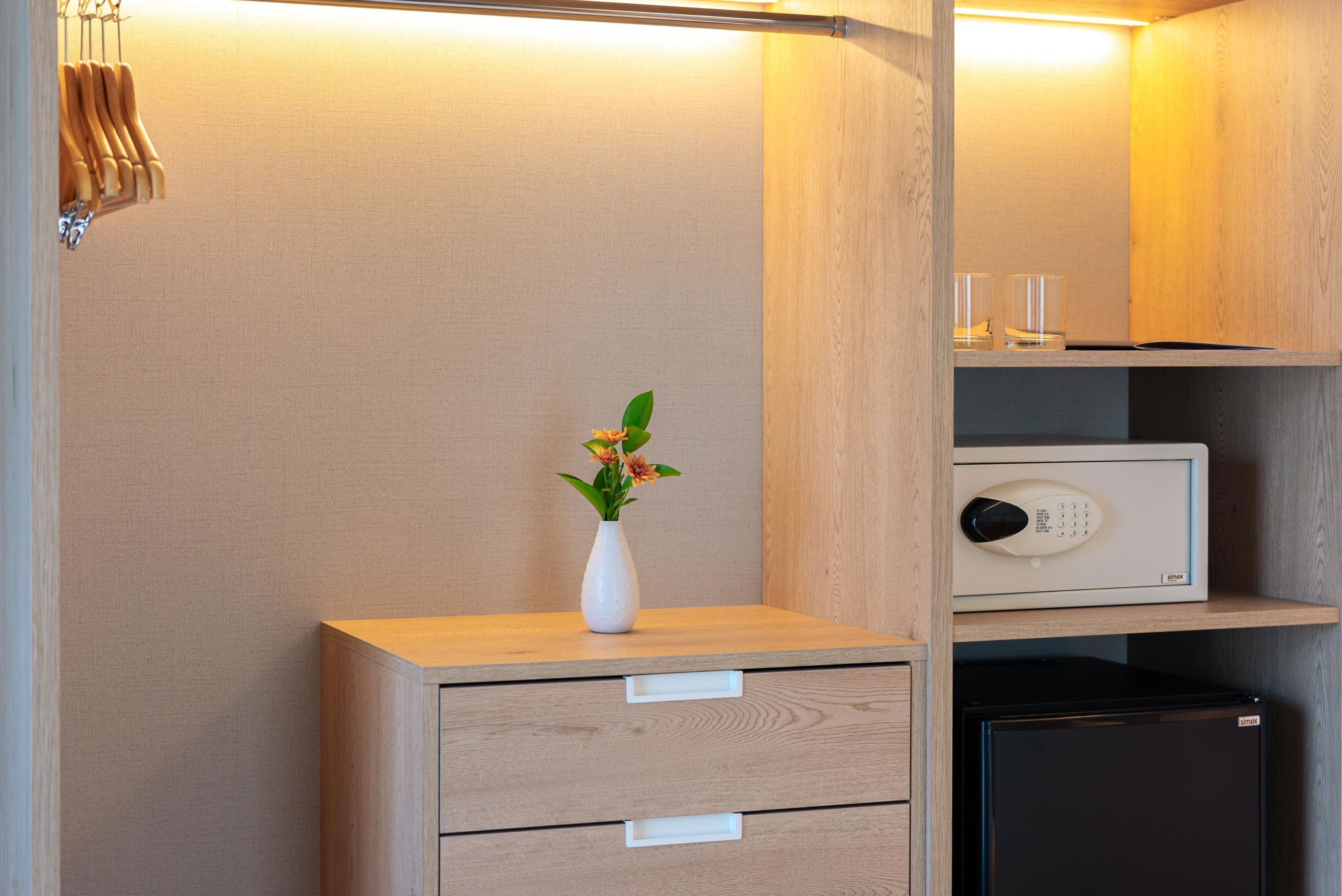 A wooden cabinet with a white vase containing flowers, a small black safe, and a drawer unit.