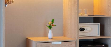 A wooden cabinet with a white vase containing flowers, a small black safe, and a drawer unit.