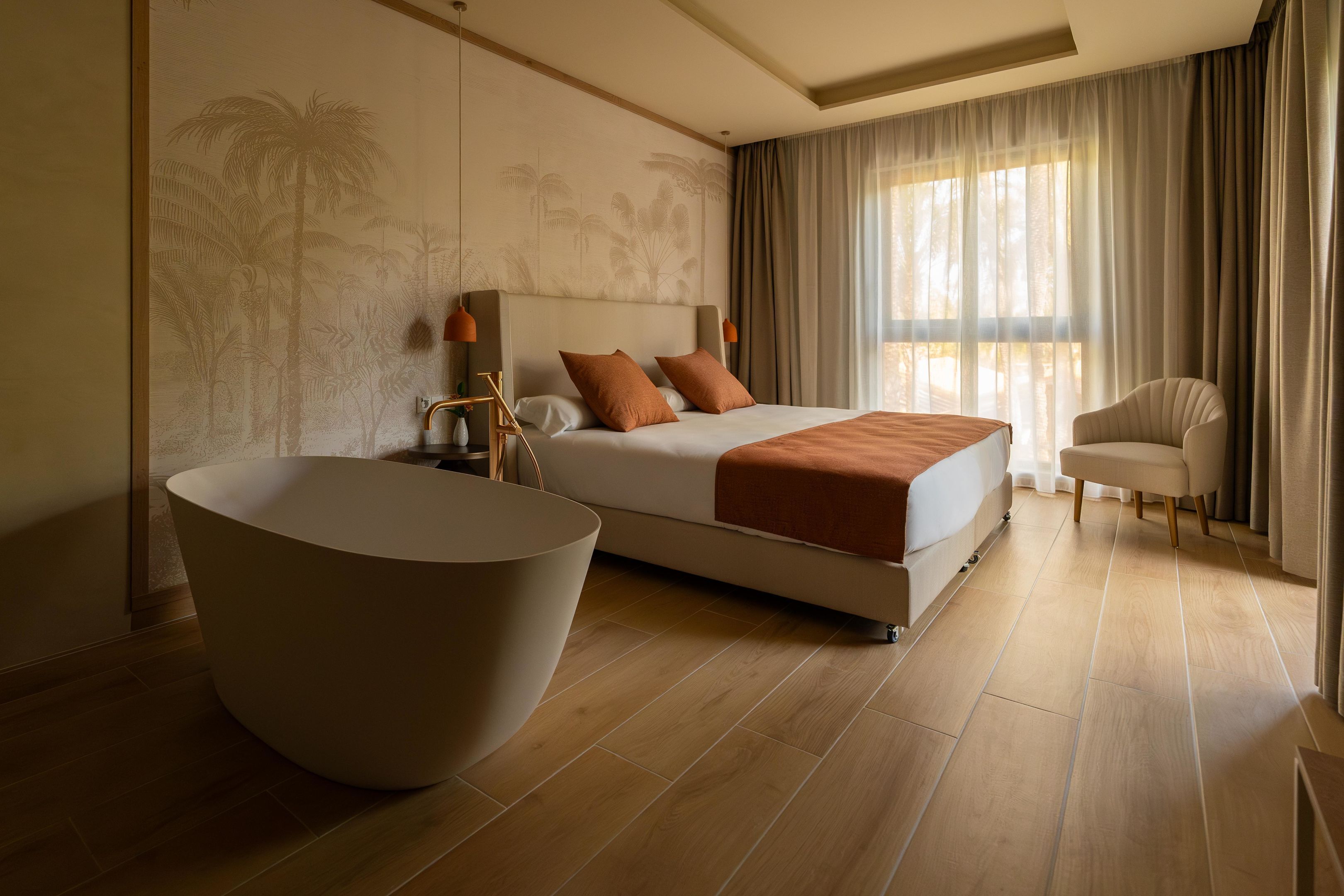 A modern hotel room with a large bed, a round bathtub, and a seating area.