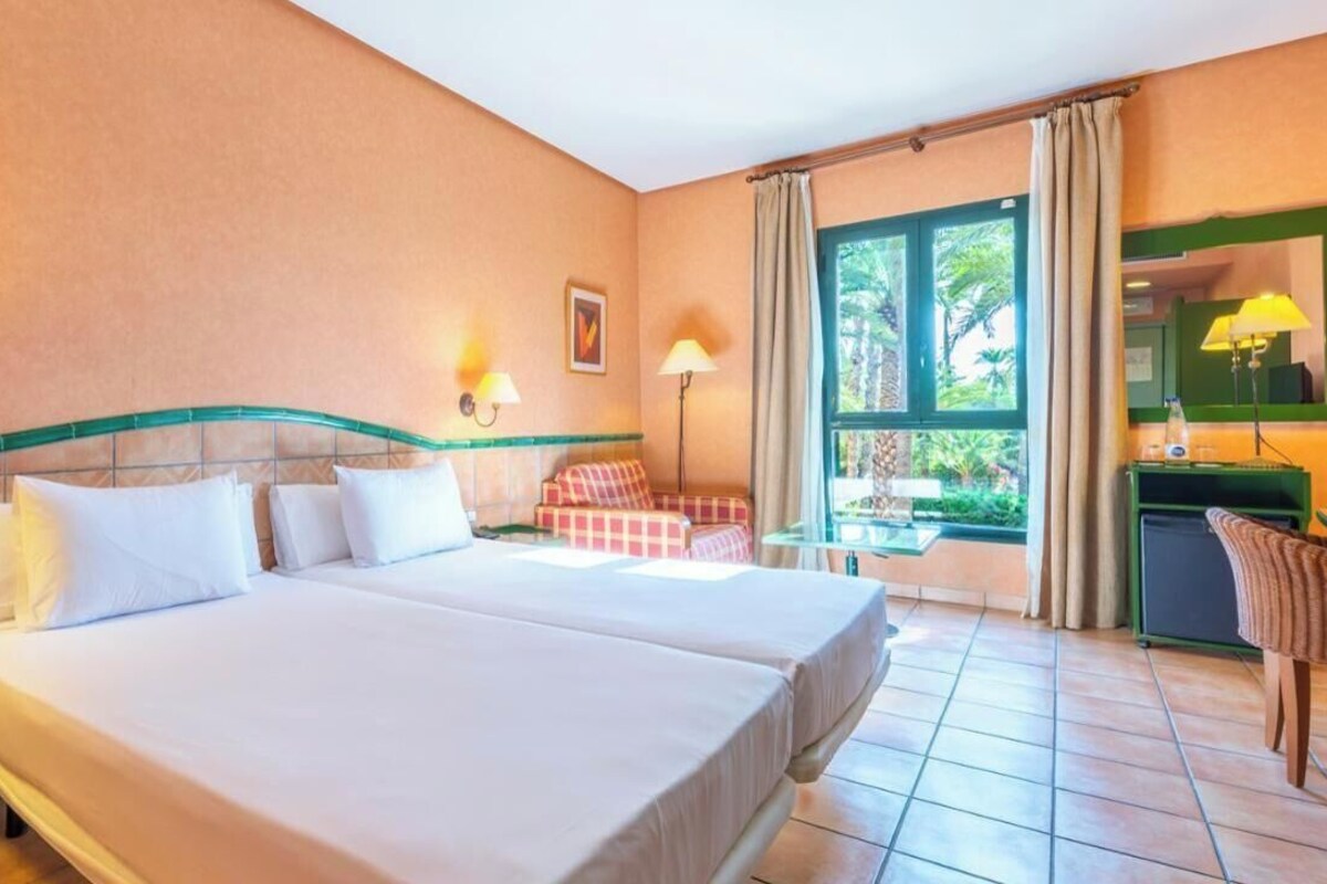 A hotel room with two beds, a desk, a chair, and a window with curtains.